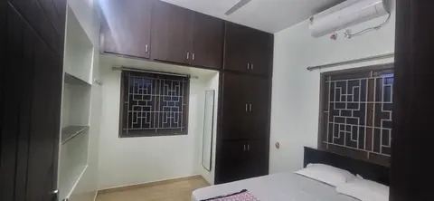 Master bedroom with a cot, wall-mounted split air-conditioner, wardrobe and loft cabinets, and grilled windows on two walls
