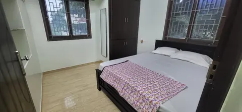Master bedroom cot between two grilled windows, with a wardrobe and standing mirror