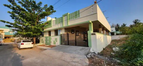 Single-storey white house with green accents behind a sliding gate, seen from the road