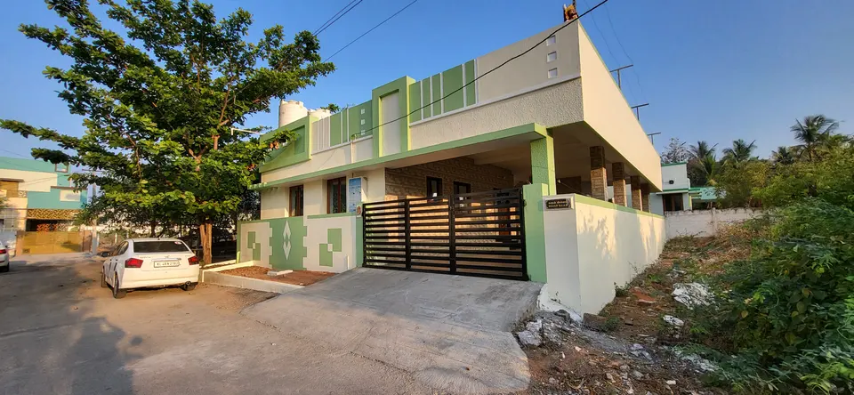 Single-storey white house with green accents behind a sliding gate, seen from the road