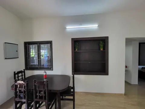 Dining table with four wooden chairs below a grilled window and a built-in shelf unit