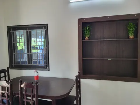 Dining table beside a grilled window and a dark wood shelf unit with plants