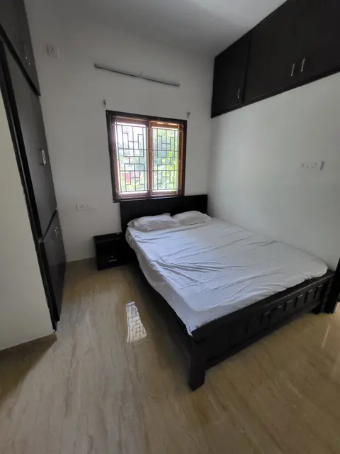 Master bedroom with a dark wood cot made up in white linen below a grilled window