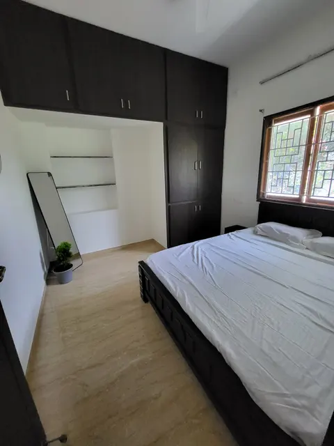 Cot beside a grilled window, with a tall wardrobe and standing mirror