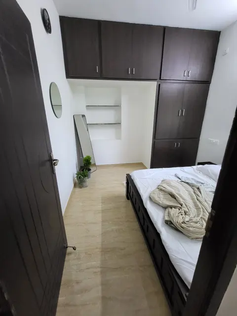 Master bedroom with loft cabinets, tall wardrobe, open wall shelves and a wooden cot