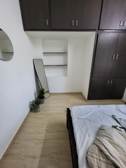 Wooden cot facing a built-in wardrobe, open shelves and a round wall mirror