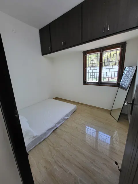 Floor mattress below a grilled window with loft cabinets above