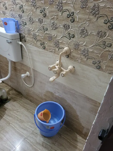 Wall mixer tap and hand shower above a bucket on the tiled floor